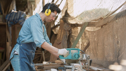 A male carpenter using a circular saw to cut wood for making new furniture at wood workshop....