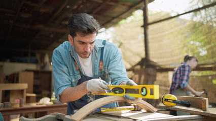 A male carpenter using precision level making new furniture at wood workshop. Carpenter using...