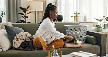 Laundry, housework and a black woman folding washing on a sofa in the living room of her home to...