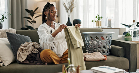 Laundry, housework and a black woman folding washing on a sofa in the living room of her home to tidy. Smile, relax and a happy young housewife cleaning her apartment for housekeeping or hygiene - obrazy, fototapety, plakaty