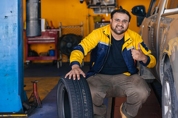 Portrait Indian man worker in garage auto mechanic happy work car service replace tyre vehicle...