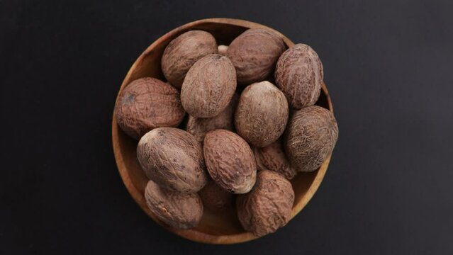whole nutmeg spice in bowl top view on black surface rotation