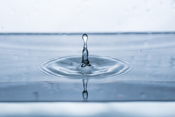 Captivating water droplet reflects on a white surface, forming an intriguing splash shape. Ideal...