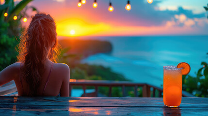 A woman enjoys a serene sunset view over the ocean, with a refreshing orange cocktail on the table, creating a peaceful and idyllic vacation moment.