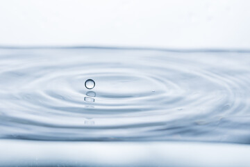 A mesmerizing water droplet hovers above a tranquil water surface against a pristine white...