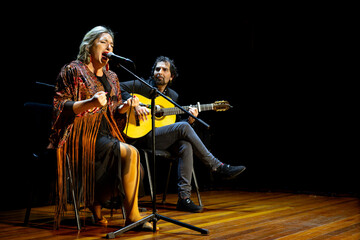 Emotive flamenco singer with accompanying guitarist on stage, copy space.