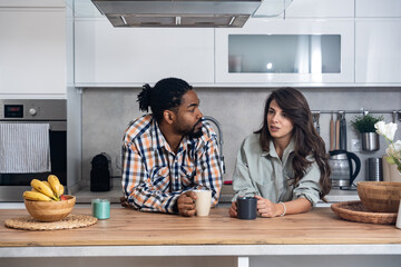 Simple living. Young couple drinking their first morning coffee in the kitchen discussing improving...