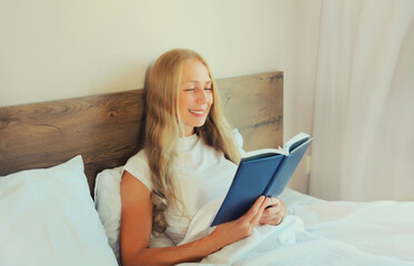 Happy middle aged woman reading book lying on the bed at home