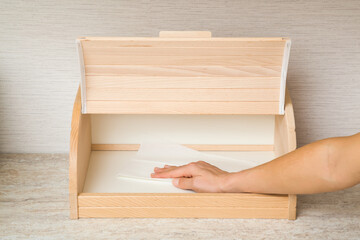 Young adult woman hand holding dry white paper napkin and wiping inside wooden bread box on table top at home kitchen. Closeup. Regular cleanup. Front view.