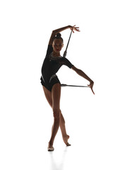 Artistic, talented, beautiful teen girl, rhythmic gymnast performing in black costume with clubs against white studio background. Concept of sport, beauty and grace, competition, art, youth, hobby