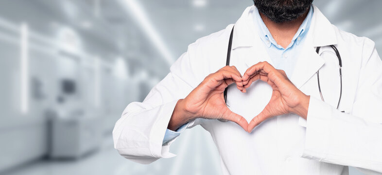 A compassionate man doctor in a white coat forming a heart shape with his hands in a hospital