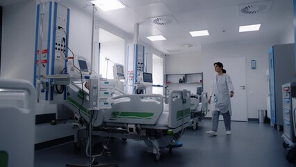Emergency room with modern equipment in clinic. Sick elderly patient in oxygen mask sleeps in bed after successful surgery. Nurse uses hospital monitor. Intensive care department in medical facility. - Powered by Adobe
