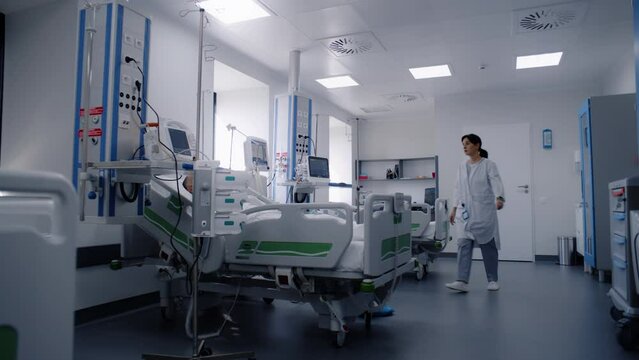 Emergency room with modern equipment in clinic. Sick elderly patient in oxygen mask sleeps in bed after successful surgery. Nurse uses hospital monitor. Intensive care department in medical facility.