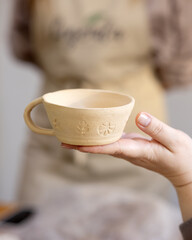 Handmade ceramic mug without glaze on a woman's palm. Blurred background