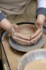 student aligns the walls of a clay cup with his own hands on a potter's wheel