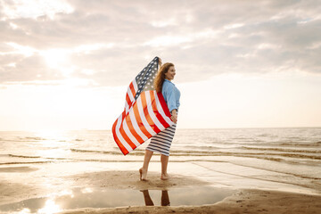 Happy woman holding United States of America flag and running  on the beach at sunset. Patriotic...