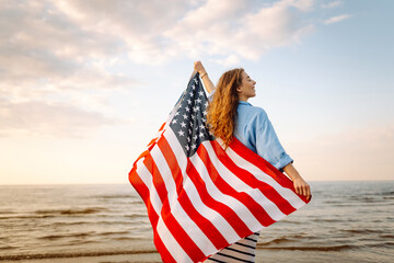 Happy woman holding United States of America flag and running  on the beach at sunset. Patriotic...