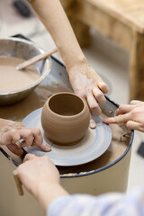 teacher helps the student to remove the finished work from the potter's wheel with the help of string cutter