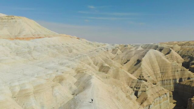 A man stands on the ridge of desert chalk mountains. A guy shooting a photo of the landscape on his smartphone. Aerial photography. Altyn-Emel National Park