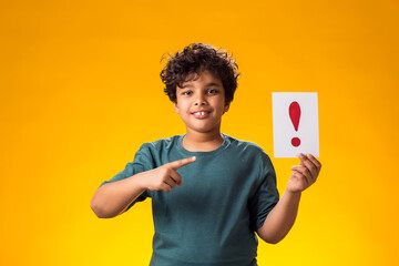 Kid boy holding exclamation point card and pointing finger at it. Education and curiosity concept