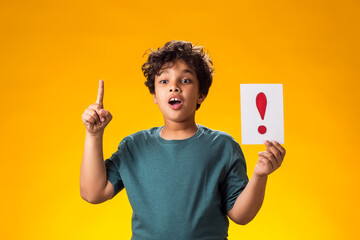 Surprised kid boy holding exclamation point card and showing finger up. Education and curiosity...