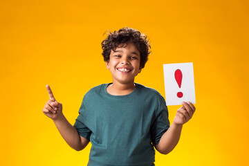 Surprised kid boy holding exclamation point card and showing finger up. Education and curiosity concept
