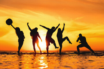 Group of young friends are having fun at sunset beach. Funny silhouettes of happy tourists