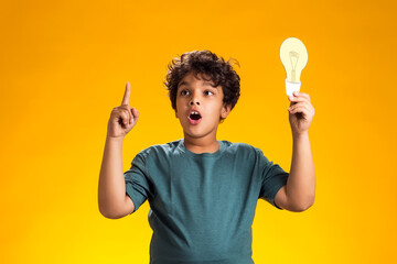 Surprised child boy holding paper bulb and holding finger up. Success, motivation, winner, genius,...