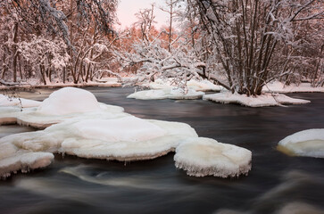 Winter river landscape, Partially frozen river in snowy forest illuminated by reflected light of...