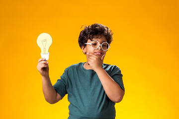 Pensive child boy holding paper bulb. Success, motivation, winner, genius, idea concept