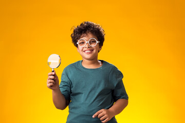 Child boy holding magnifier over yellow background. Education and curiosity concept