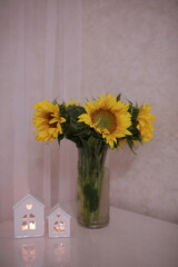 a bouquet of sunflowers stand in a vase at the workplace near the laptop. candles in the shape of a house. aesthetic workplace at home.
