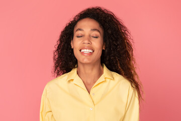 Joyful black woman with closed eyes smiling, posing in yellow shirt