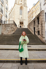 Fototapeta na wymiar urban vibes, happy woman in trendy sunglasses with smartphone walking on city street in Vienna
