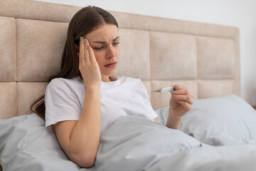 Sick woman in bed checking temperature with thermometer