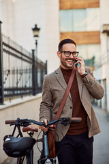 A smiling businessman pushing a bicycle and having a phone call. walking on a street.