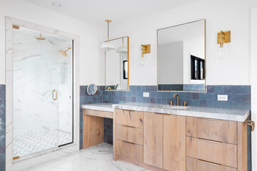 A luxurious bathroom with a wood vanity cabinet, blue tiles on the walls, gold accented lights and mirrors, and a large walk-in shower lined with marble tiles. No brands or labels. - obrazy, fototapety, plakaty