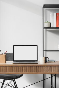 Laptop computer with empty blank white mockup screen over modern living room design. Home office, workplace, working or studying from home, distance learning, business concept