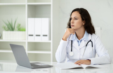 Pensive beautiful millennial woman doctor sitting at her office - obrazy, fototapety, plakaty