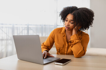 A thoughtful young African American woman with curly hair wearing a mustard shirt