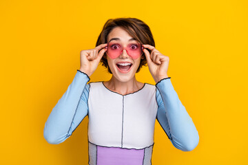 Photo of positive impressed woman wear top hands arms heart eyeglasses open mouth isolated yellow...