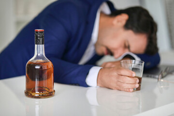 An exhausted or distressed businessman in a blue suit is resting his head on a desk