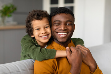Cheerful black son hugs father from behind with bright smiles