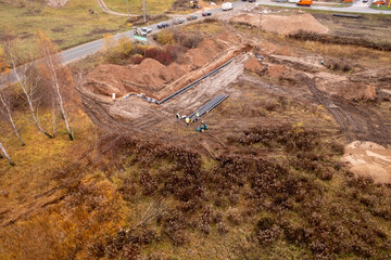 Drone photography of sewage pipe being lade down i a ditch by a road during autumn day
