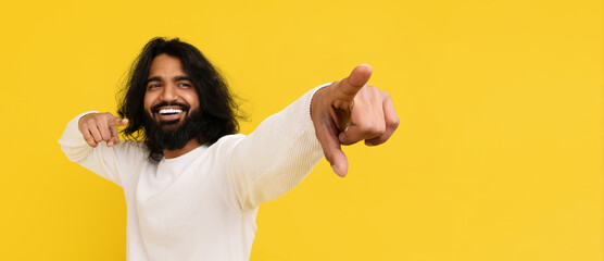 Cool bearded young hindu guy pointing at copy space