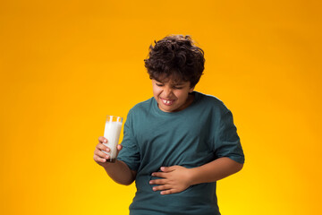 Dairy intolerant unhappy child boy holding glass of milk feeling stomach pain over yellow...