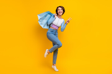 Fototapeta na wymiar Full length portrait of excited pretty person hold shop bags demonstrate v-sign isolated on yellow color background