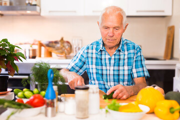 Senor man preparing fresh vegetable salad at home in the kitchen