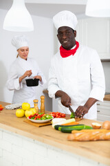 Professional chef in white uniform working with female assistant in private kitchen