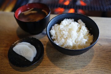 囲炉裏の前で食べる白米、たくあん、味噌汁